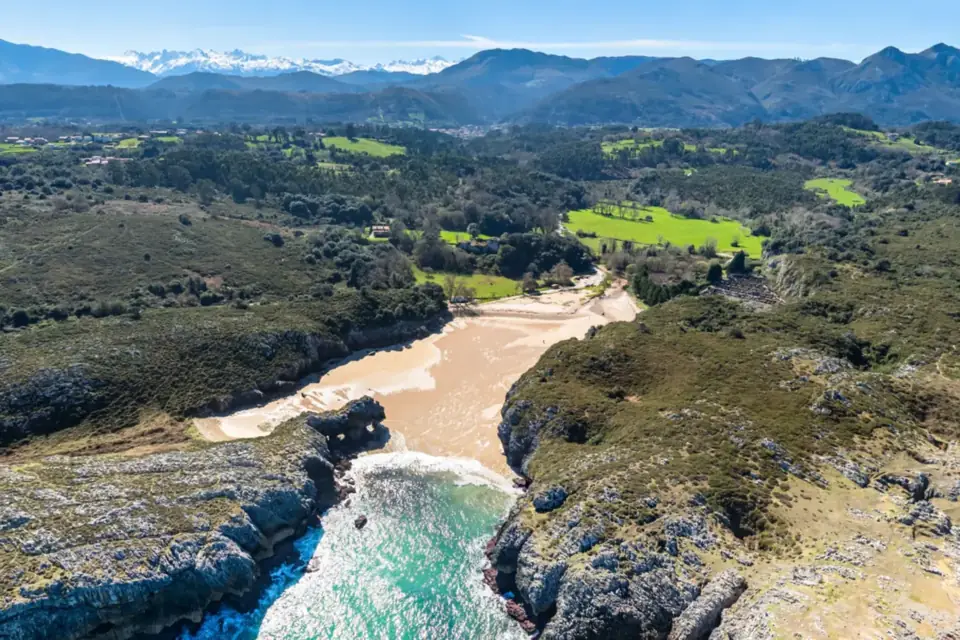 Playa de Cuevas del Mar, la cala entre acantilados calizos con los Picos de Europa nevados al fondo