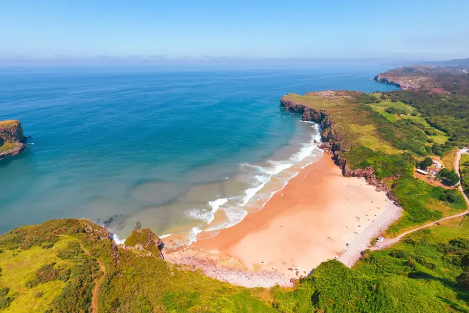 Playa de Andrín, la concha de arena rojiza con la rompiente y la punta que la cierra