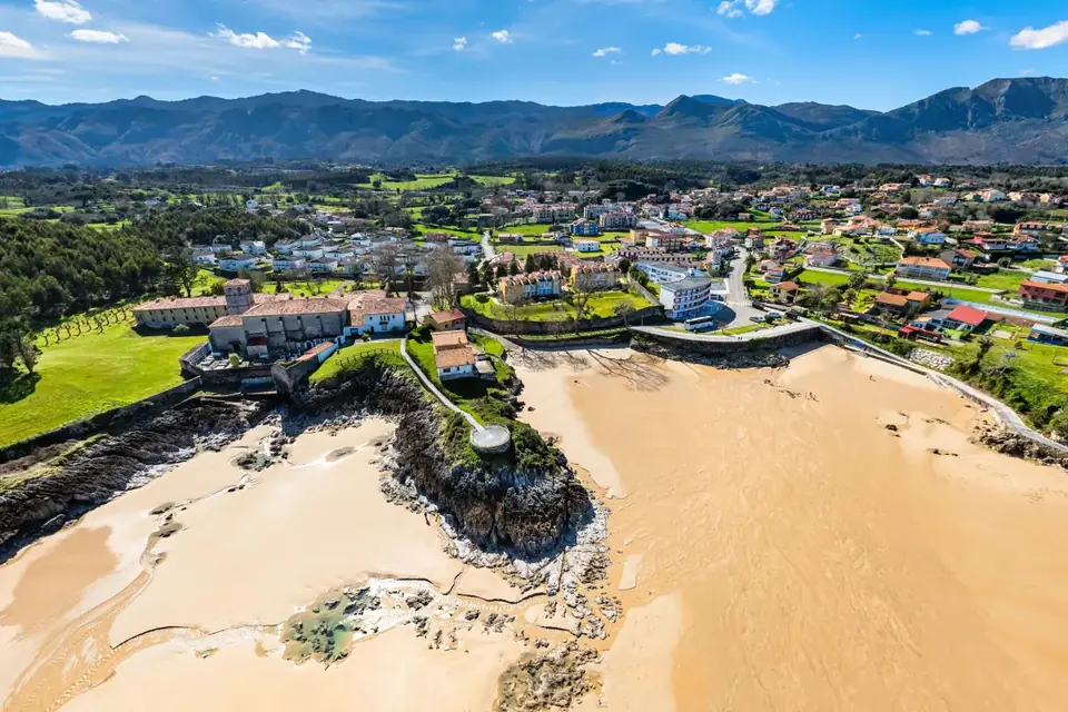 Playa de Las Cámaras, en Celorio, con los arenales en bajamar, el pueblo y la sierra del Cuera