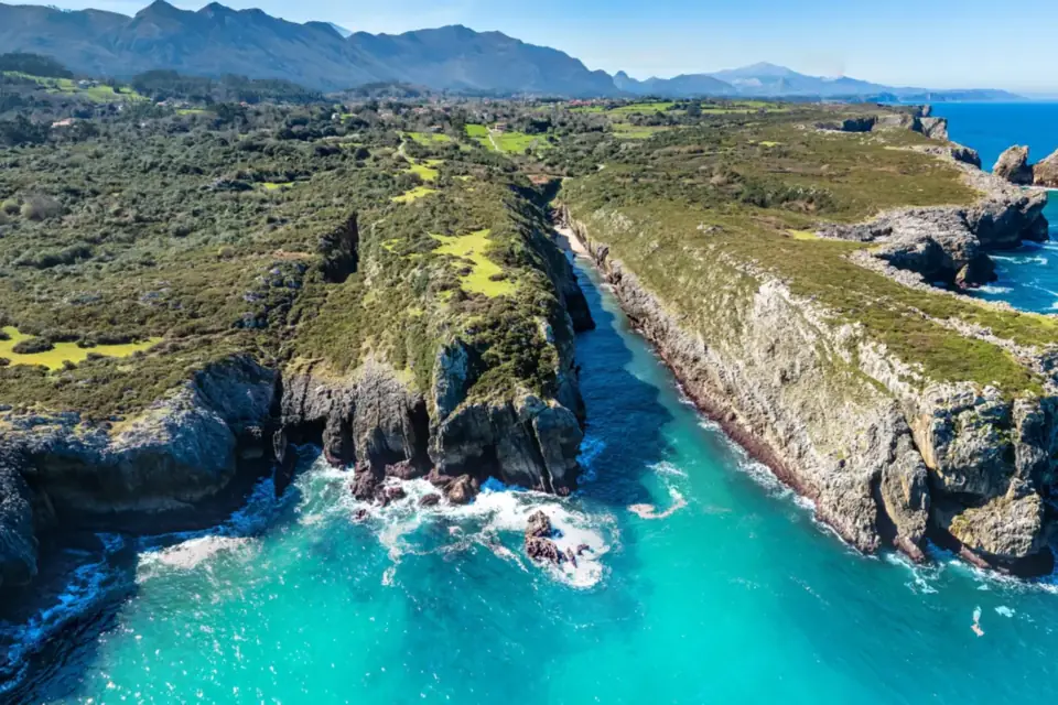 Entrante estrecho entre paredes calizas, con agua turquesa y los Picos de Europa al fondo, en la zona de La Canal