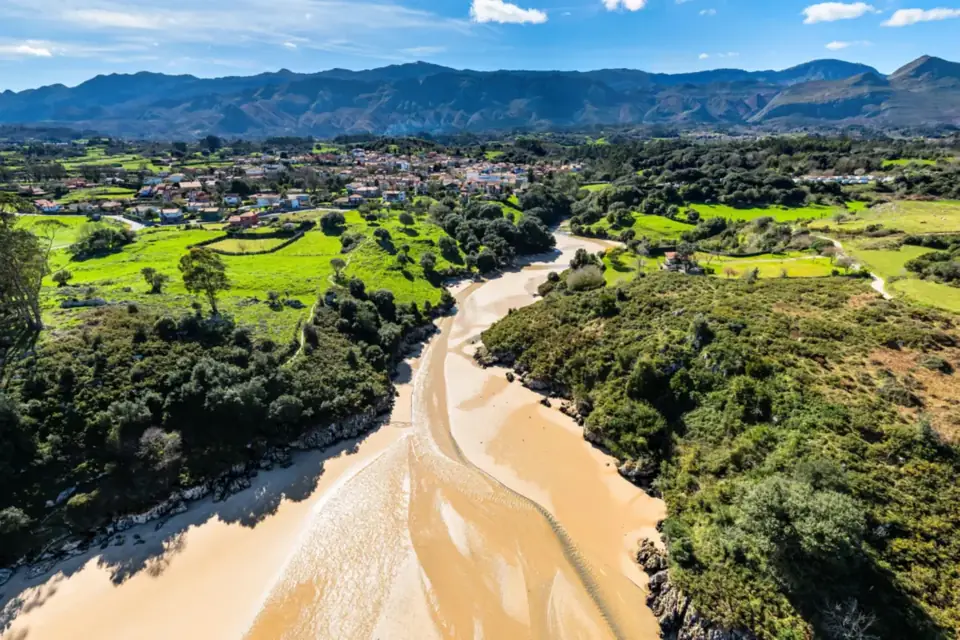 Playa de Poo, la ría de arena entre arbolado, el pueblo y la sierra del Cuera