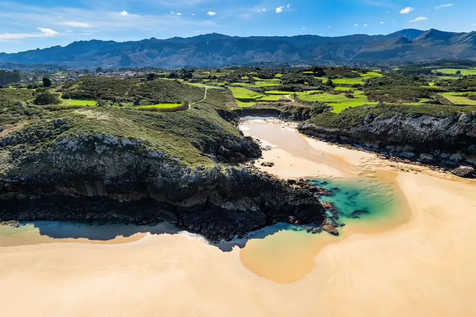 Playa de San Martín, arenal en bajamar con una poza turquesa bajo el acantilado